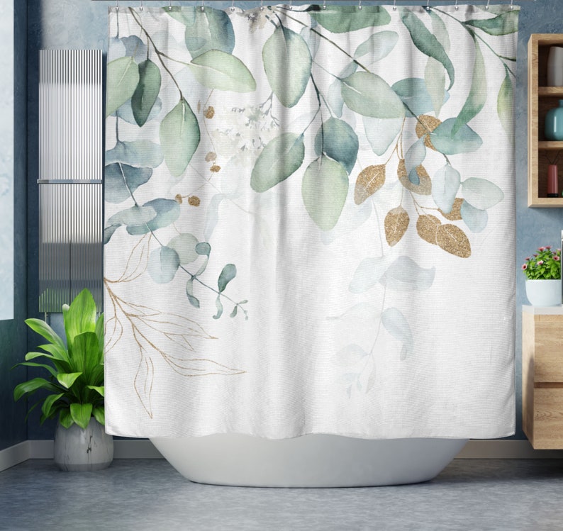 May include: White shower curtain with a watercolor design of green and gold eucalyptus leaves. The leaves are in various shades of green and blue, with gold glitter accents. The curtain is hanging in a bathroom.