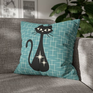 May include: A teal blue throw pillow with a black silhouette of a cat with white stars. The background of the pillow has a white grid pattern.