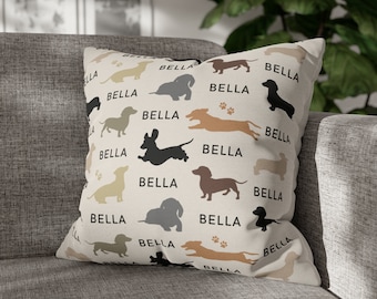 May include: A beige throw pillow with a repeating pattern of black dachshund silhouettes and the name "Bella" printed in black.