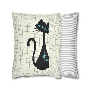 May include: A pair of decorative throw pillows. One pillow features a black cat with blue eyes and turquoise stars on a cream background with a blue grid pattern. The other pillow is gray with white stripes.