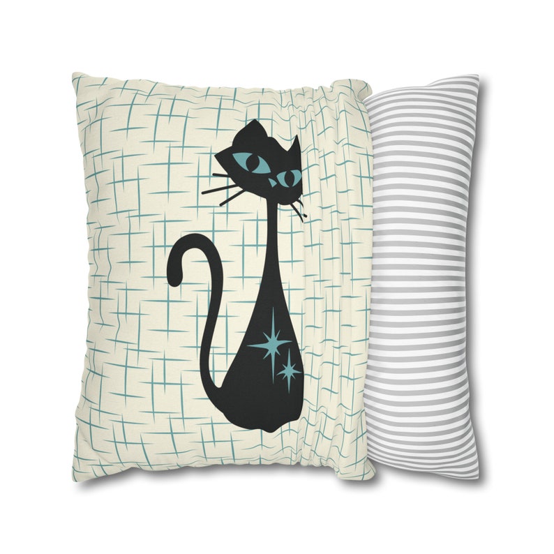 May include: A pair of decorative throw pillows. One pillow features a black cat with blue eyes and turquoise stars on a cream background with a blue grid pattern. The other pillow is gray with white stripes.