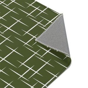 May include: A green and white geometric patterned rug with a white stitched border. The rug is folded to show the gray backing.