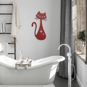 May include: Red metal cat wall decor with a starburst design. The cat is in a standing position with its tail curled around its body. The cat is mounted on a white wall above a white bathtub.
