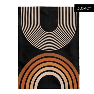 May include: A black throw blanket with a geometric design featuring two sets of concentric arches in beige, orange, and brown. The blanket measures 30x40 inches.