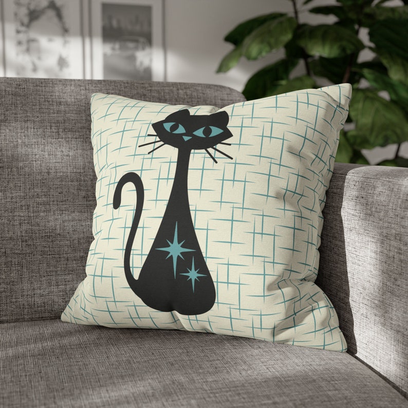 May include: A black cat with blue eyes and turquoise stars on a cream pillow with a blue and white grid pattern.