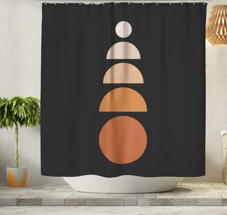 May include: Black shower curtain with a geometric design. The design features a series of stacked shapes in a vertical line: a white circle, two half-circles in beige, a half-circle in orange, and a large orange circle at the bottom. The curtain is hanging in front of a white bathtub.