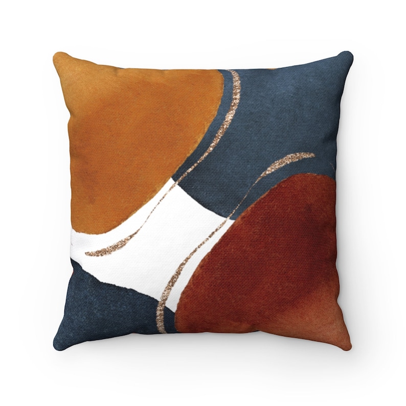 May include: A square throw pillow with an abstract design featuring overlapping circles in shades of orange, brown, blue, and white with gold accents.