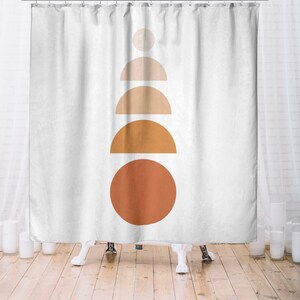 May include: White shower curtain with a minimalist design. The design features a stack of geometric shapes in shades of orange and beige, including a circle, semi-circles, and a smaller circle at the top. The curtain hangs from a metal rod.