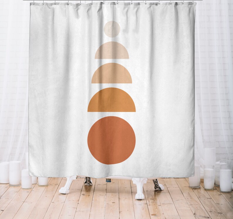 May include: White shower curtain with a minimalist design. The design features a stack of geometric shapes in shades of orange and beige, including a circle, semi-circles, and a smaller circle at the top. The curtain hangs from a metal rod.
