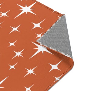 May include: A close-up of a rust-colored rug with a white starburst pattern. The rug is folded over to show the gray backing.