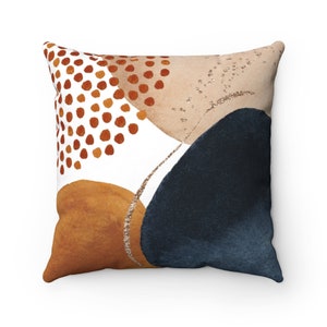 May include: A decorative throw pillow with an abstract design featuring a white background with brown, orange, and blue shapes and gold glitter accents.