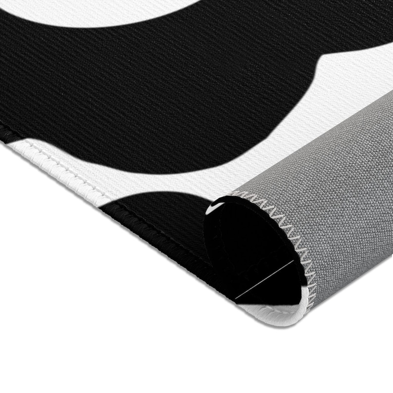 Peut inclure: Tapis &agrave; motifs noirs et blancs avec un dos gris. Le tapis a un design g&eacute;om&eacute;trique avec de grandes formes arrondies.