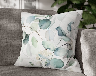 Op de afbeelding: Een wit kussen met een aquarelontwerp van groene en blauwe eucalyptusbladeren.