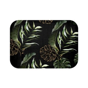 Puede incluir: Alfombra de ba&ntilde;o negra con un patr&oacute;n de hojas tropicales. Las hojas son verdes y doradas y tienen un efecto acuarela.