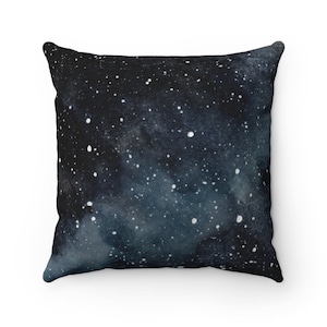 May include: A black and blue throw pillow with a watercolor galaxy print. The pillow features a dark blue background with white stars and a light blue nebula.