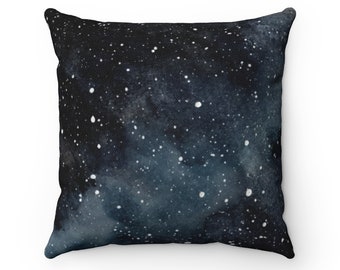May include: A black and blue throw pillow with a watercolor galaxy print. The pillow features a dark blue background with white stars and a light blue nebula.