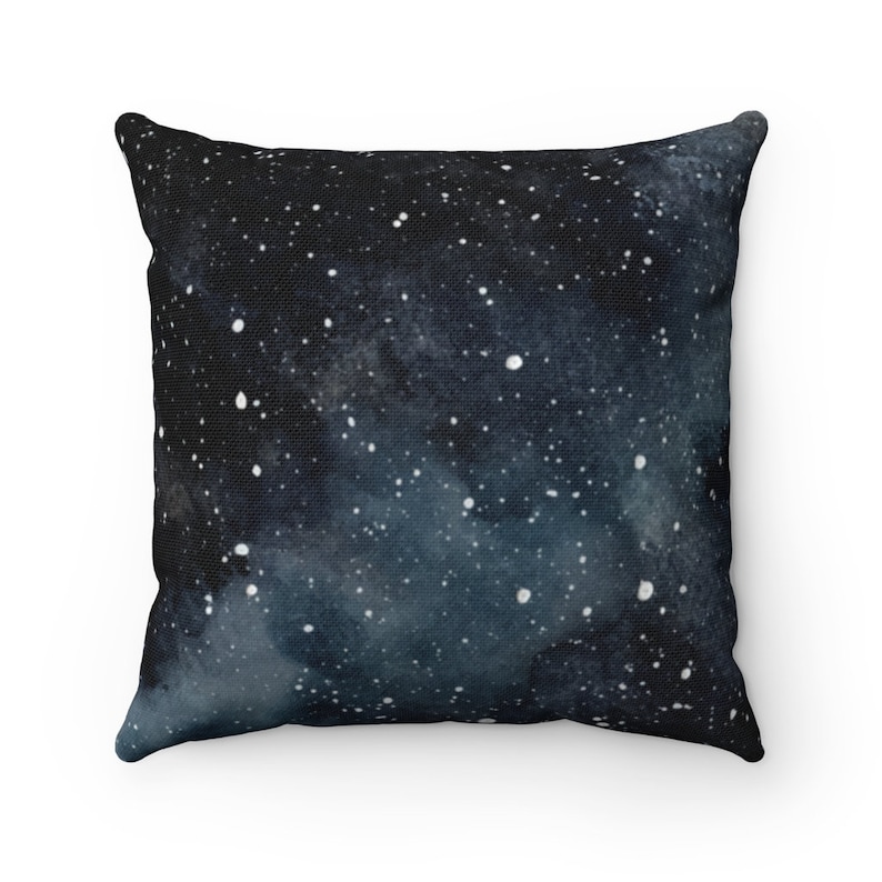 May include: A black and blue throw pillow with a watercolor galaxy print. The pillow features a dark blue background with white stars and a light blue nebula.
