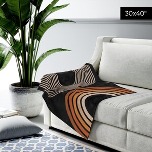 May include: A black and brown throw blanket with a geometric rainbow design. The blanket is 30x40 inches and is draped over a white couch.