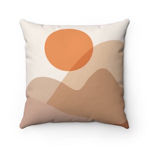 May include: A throw pillow with a minimalist design featuring a large orange sun and abstract brown hills on a white background.