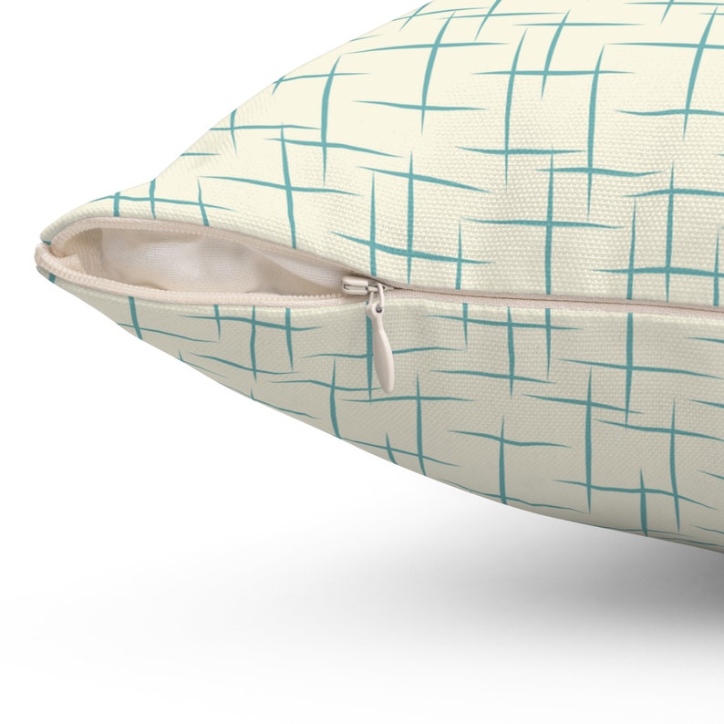 May include: A cream-colored pillow with a zipper closure. The pillow has a teal geometric pattern.