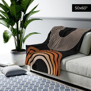 May include: A black throw blanket with a geometric pattern of orange, brown, and white stripes and arcs. The blanket is 50x60 inches and is draped over a couch.