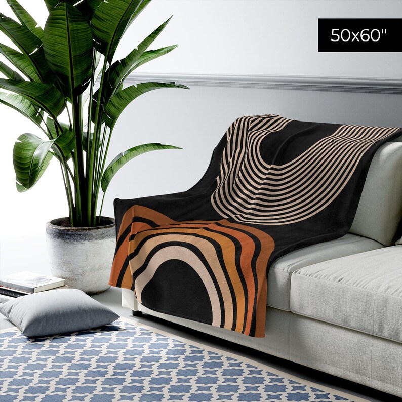 May include: A black throw blanket with a geometric pattern of orange, brown, and white stripes and arcs. The blanket is 50x60 inches and is draped over a couch.