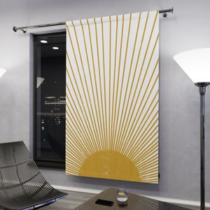 Puede incluir: Una cortina blanca con un diseño de sol amarillo. El sol está formado por finas líneas amarillas que irradian desde un círculo amarillo en el centro. La cortina está colgada en una ventana.