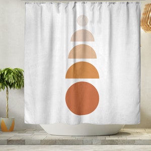 May include: White shower curtain with a minimalist design. The design features a stack of geometric shapes in shades of orange and tan, including circles and semi-circles. The curtain is hanging in front of a white bathtub.