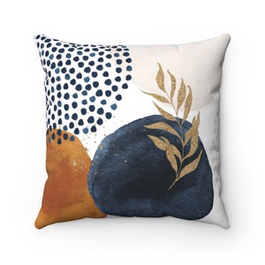 May include: A decorative throw pillow with an abstract design featuring blue, gold, and orange watercolor shapes and a gold leaf pattern.