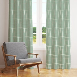 May include: A pair of green curtains with a white geometric pattern. The curtains are hanging in a window with a wooden frame. A wooden chair with a gray cushion is in the foreground.