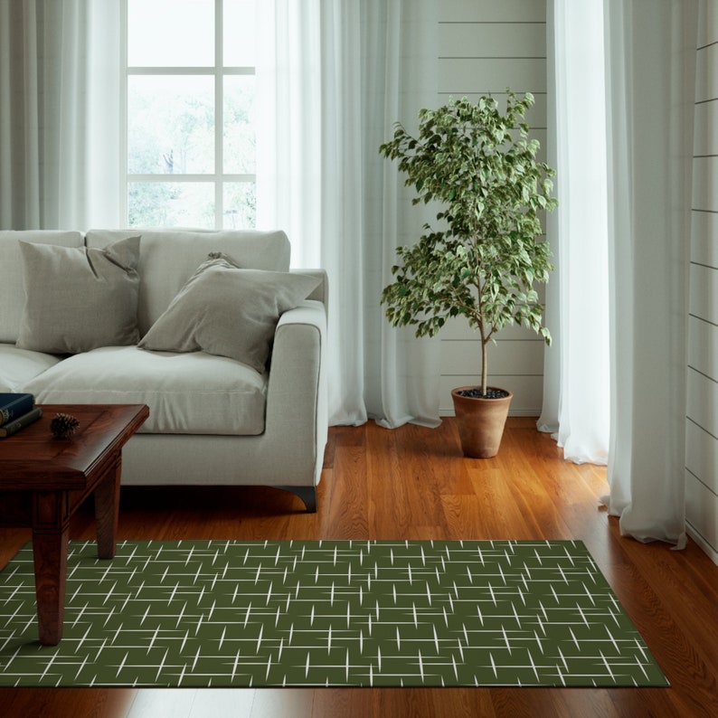 May include: A green and white geometric area rug with a modern design. The rug is placed in a living room with a white couch, a potted plant, and a wooden coffee table.