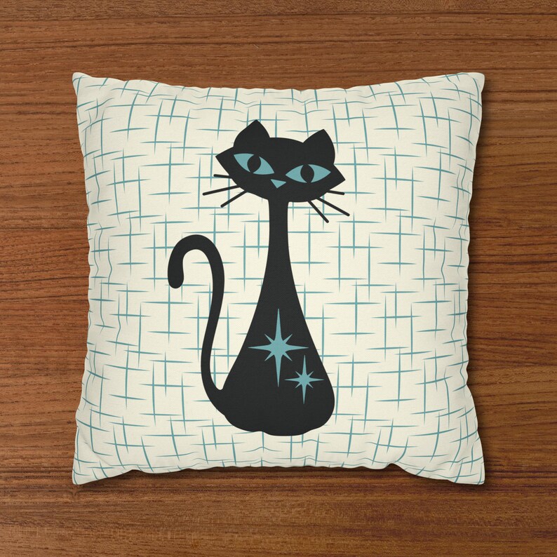 May include: A white pillow with a blue and white grid pattern. A black cat with blue eyes and stars is in the center of the pillow.