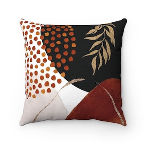 May include: A decorative throw pillow with an abstract design featuring geometric shapes, dots, and leaves in shades of brown, gold, and white on a black background.