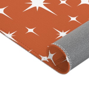 May include: A close-up of a rust-colored rug with a white starburst pattern. The rug is rolled up, showing the gray backing.