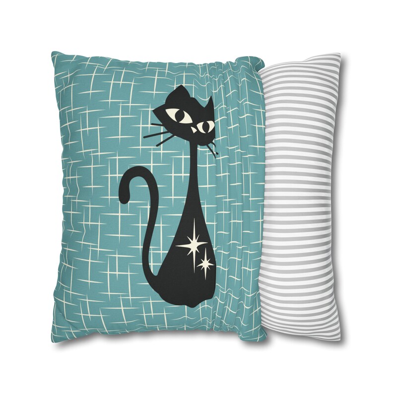 May include: A teal blue pillow with a black cat silhouette with white stars. The cat is looking to the right. The pillow has a white and gray striped pillow behind it.