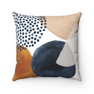 May include: A white throw pillow with an abstract design featuring blue, brown, and beige shapes. The design includes a pattern of blue dots.
