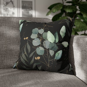 May include: A black throw pillow with a watercolor design of green leaves and gold accents.
