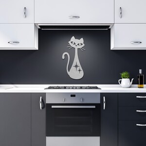 May include: A silver metal wall decor featuring a stylized cat with a starburst design. The cat is sitting on a dark gray wall in a kitchen setting.