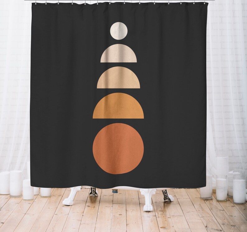 May include: Black shower curtain with a minimalist geometric design. The design features a series of stacked shapes in shades of white, beige, and orange, creating a modern and abstract pattern. The curtain is hanging in front of a white bathtub.