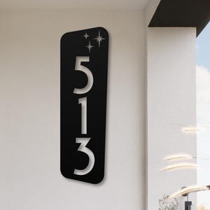 May include: Black metal house number sign with white numbers 513 and a design of stars in the top left corner.