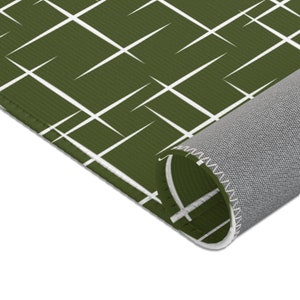 May include: A green and white geometric patterned rug with a white border. The rug is rolled up, showing the gray backing.