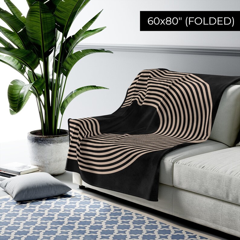 May include: A black and beige striped throw blanket folded on a couch. The blanket has a circular pattern with stripes radiating outward. The blanket is 60x80 inches when folded.
