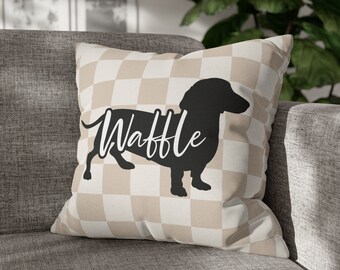 May include: A tan and white checkered throw pillow with a black silhouette of a dachshund and the word "Waffle" printed on it.
