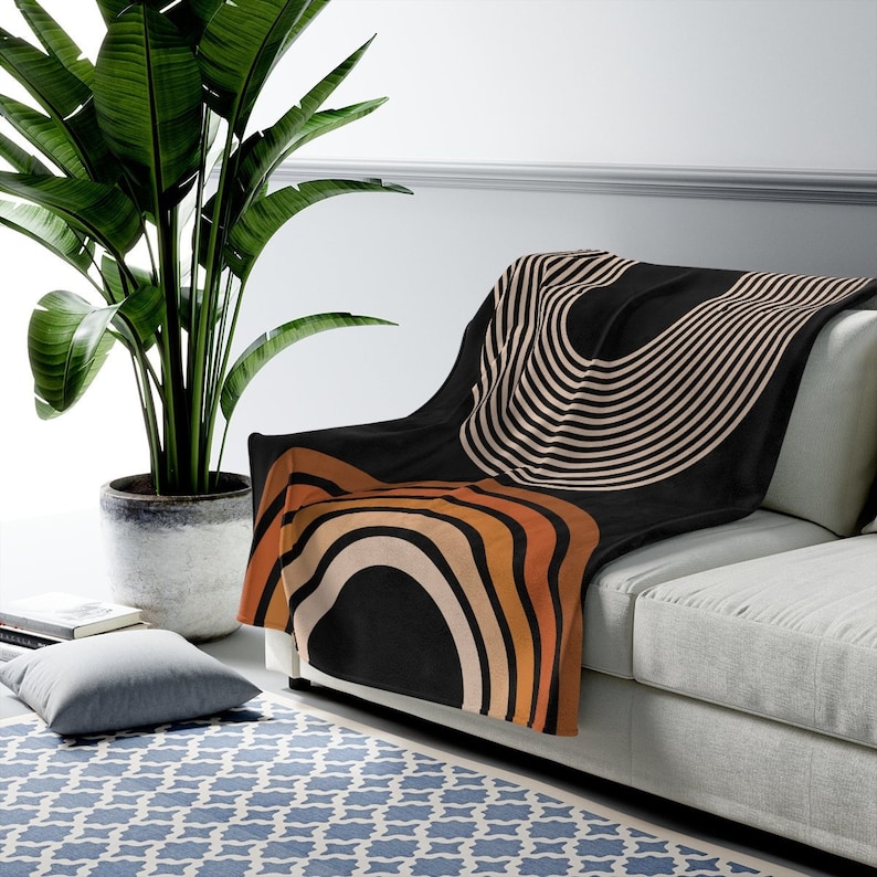 May include: A black throw blanket with a geometric pattern of orange, brown, and white stripes and curves. The blanket is draped over a light gray couch.