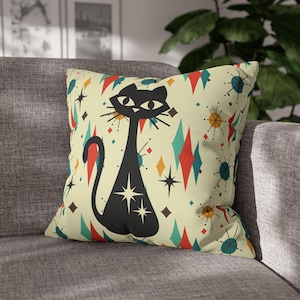 May include: A throw pillow with a retro design featuring a black cat with a starburst pattern on a cream background with red, blue, and yellow accents.