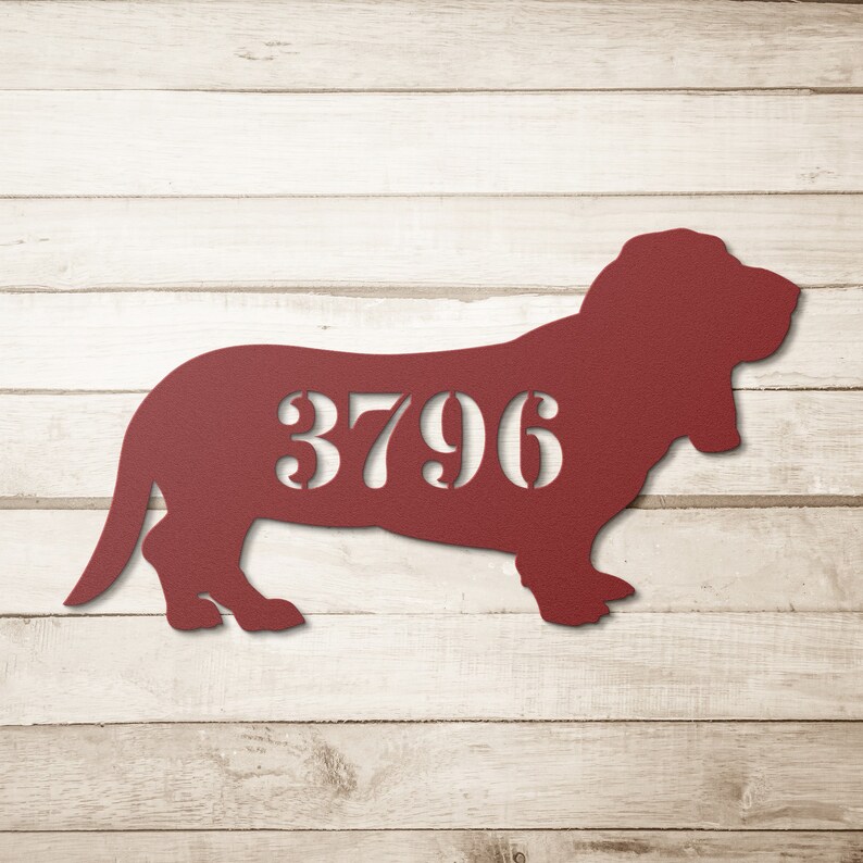 May include: A burgundy metal sign in the shape of a basset hound, with the number 3796 cut out in the center. The sign is displayed against a light wood background.