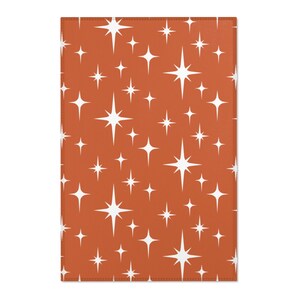 May include: A rust-colored fabric with a repeating pattern of white stars. The stars have a retro, mid-century modern design.