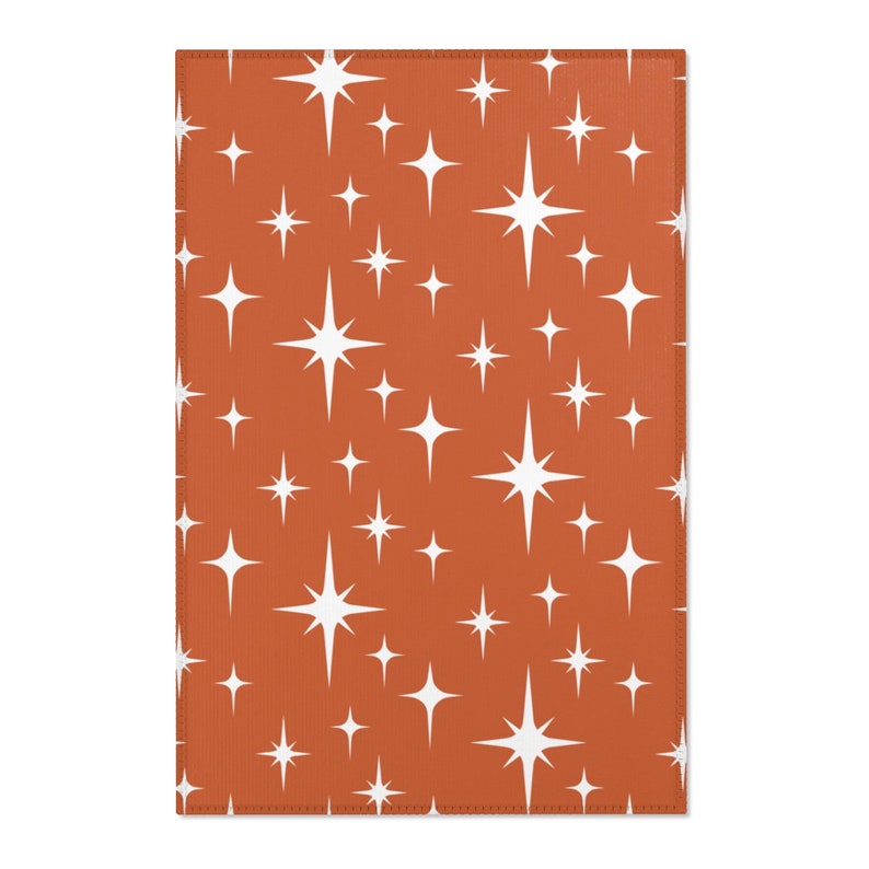May include: A rust-colored fabric with a repeating pattern of white stars. The stars have a retro, mid-century modern design.