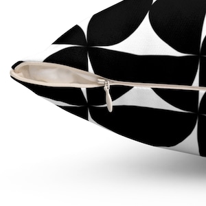 May include: A decorative pillow with a black and white geometric pattern. The pillow features a repeating design of black circular shapes against a white background. A beige zipper is visible along the edge of the pillow.