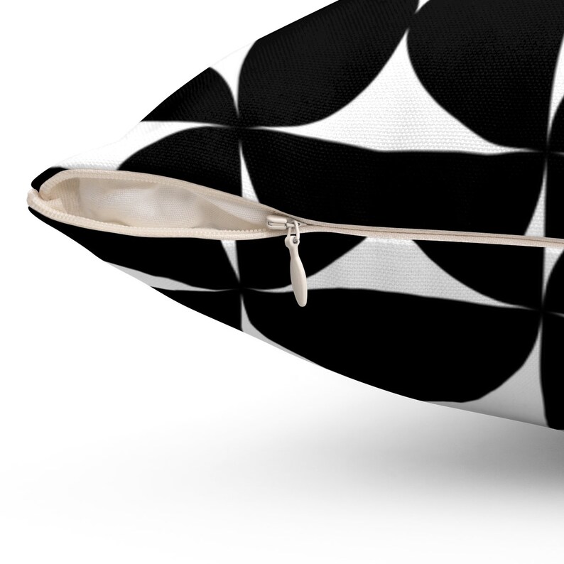 May include: A decorative pillow with a black and white geometric pattern. The pillow features a repeating design of black circular shapes against a white background. A beige zipper is visible along the edge of the pillow.